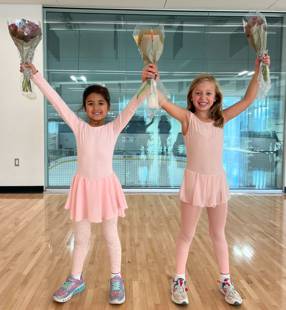 Two dance students smiling and raising their arms as the lift up bouquets of flowers inside the dance studio at Robert Crown Community Center in Evanston.