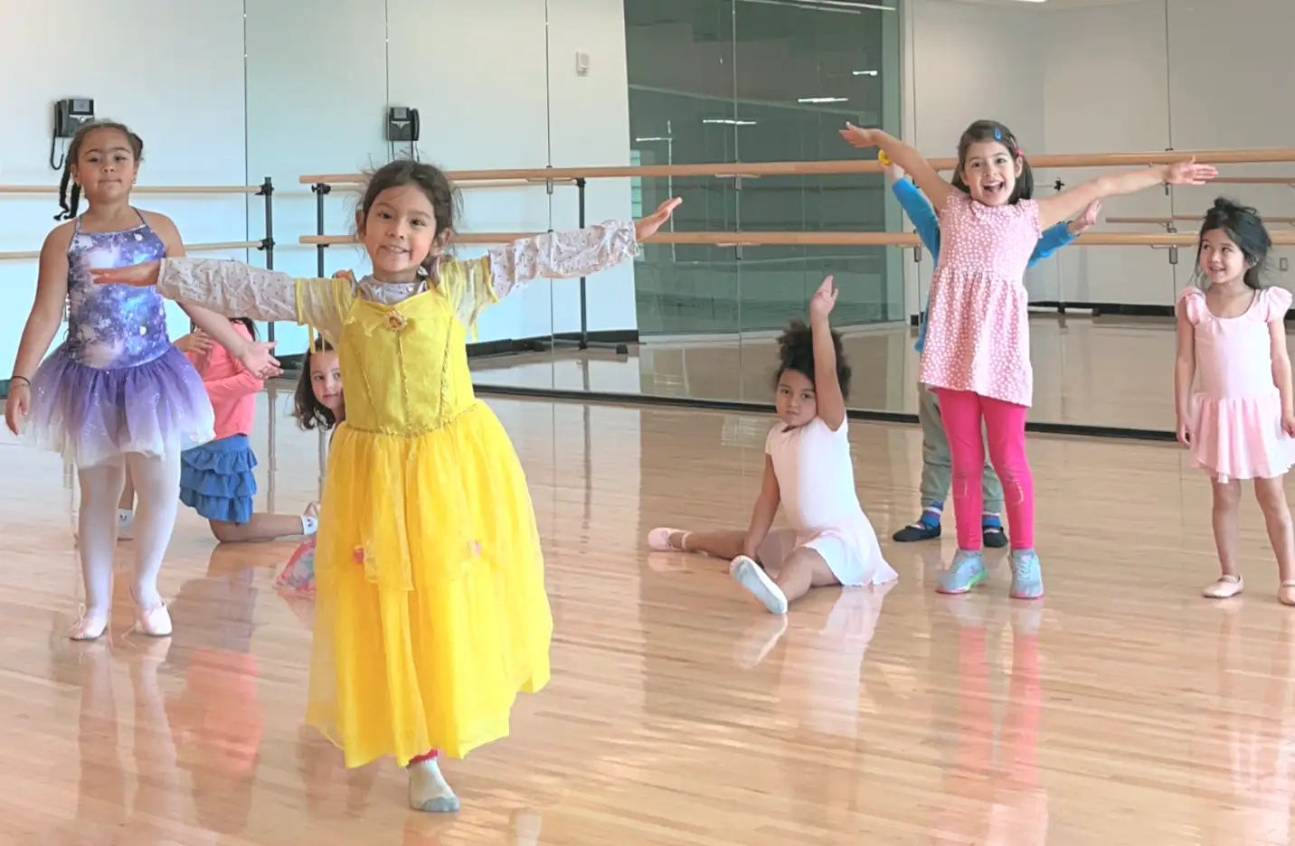 Dance class students smiling and posing in various ways and looking joyful and entertained inside the dance studio.