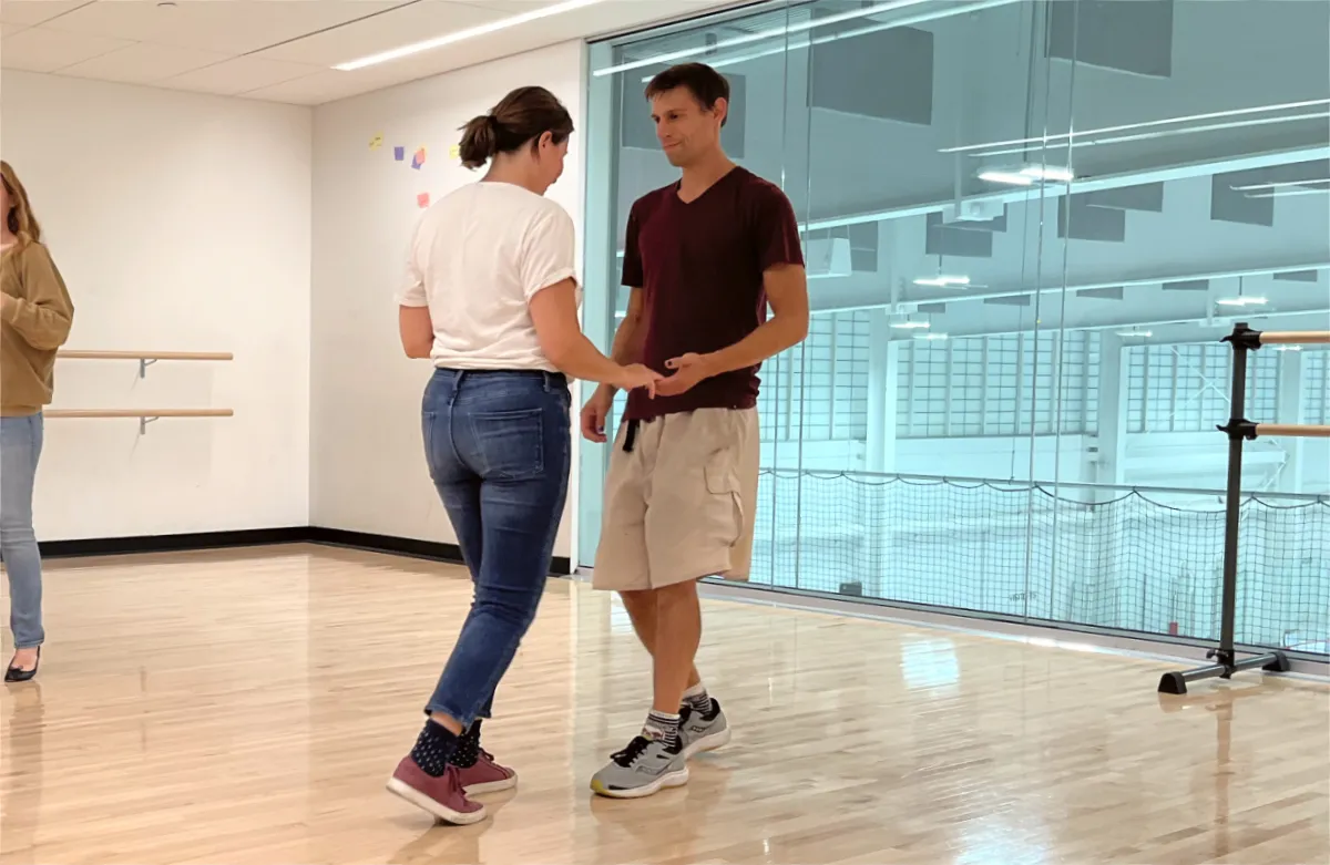 A duo of salsa dancers facing each other as they practice salsa dancing in the Robert Crown Community Center dance studio.